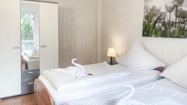 A hotel room with two beds, a mirror, a painting of flowers, and a lamp.