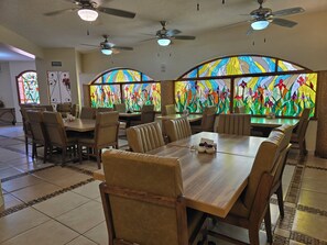 A restaurant interior with high tables, chairs, ceiling fans, and a large stained glass window. - Los Cedros Hotel Inn Ciudad Juárez  (Ciudad Juárez)