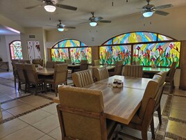 Interior de restaurante con mesas altas, sillas, ventiladores de techo y un amplio ventanal con vitrales.