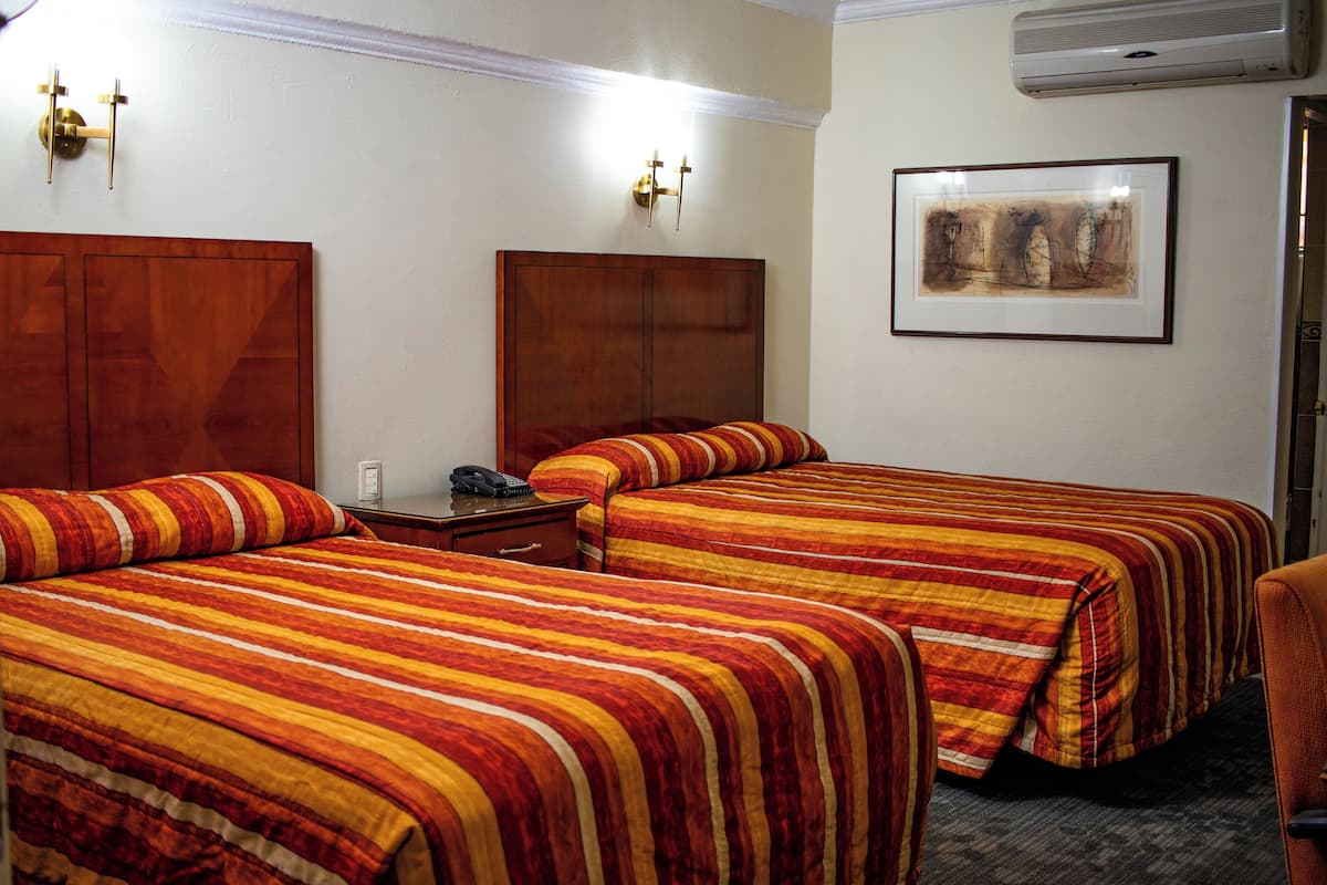 A hotel room with two beds, a wooden headboard, a bedside table with a phone, and a framed picture on the wall.