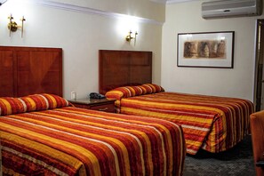 Habitación de hotel con dos camas, cabecera de madera, mesita de noche con un teléfono y un cuadro en la pared.