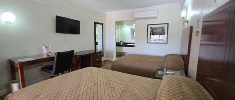 A hotel room with two beds, a desk, a chair, a television, and a bathroom visible through an open door.