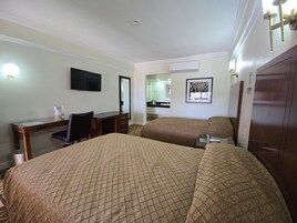 Habitación de hotel con dos camas, un escritorio, una silla, un televisor y un baño visible a través de una puerta abierta.