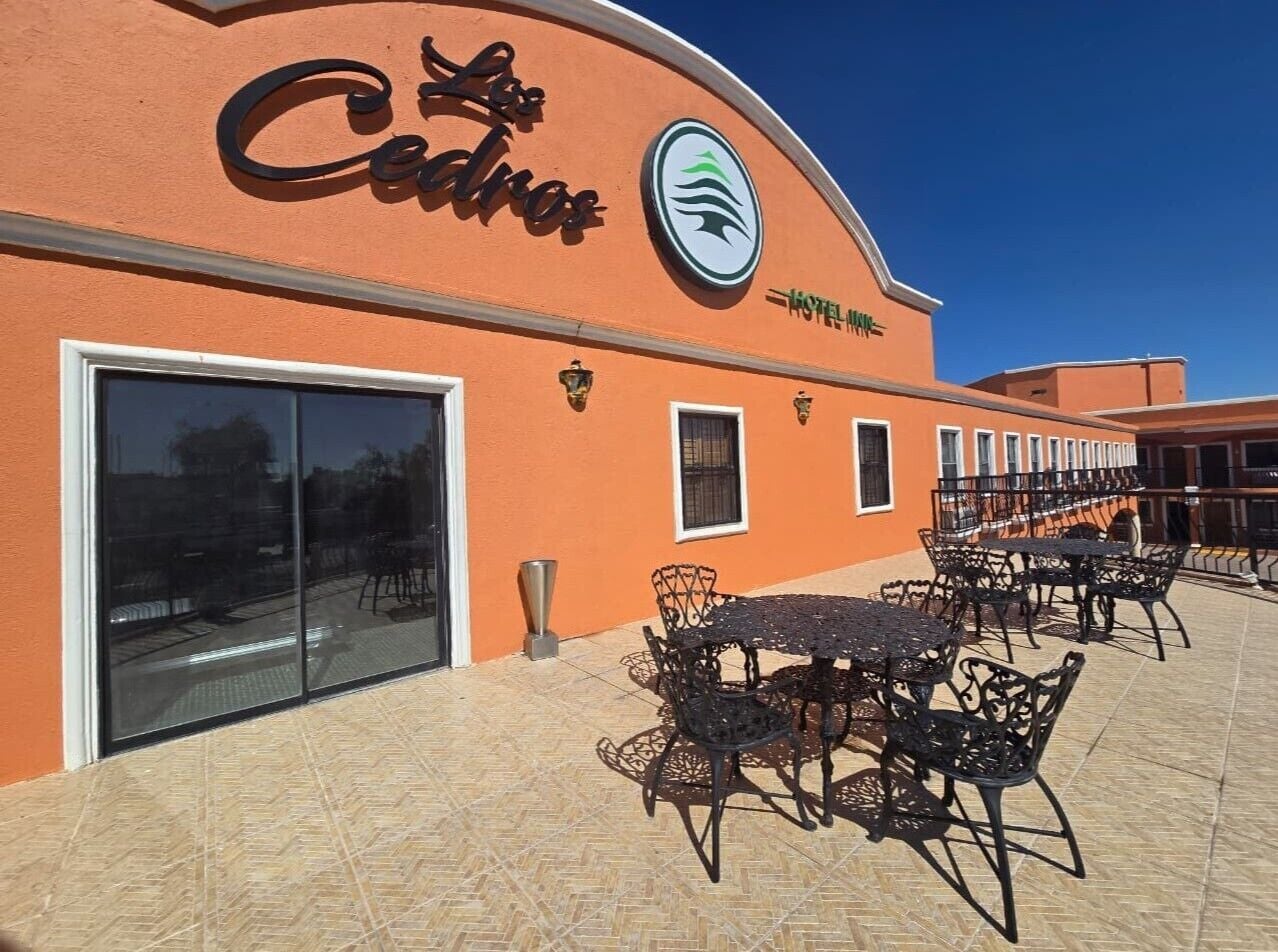 A hotel exterior with a large glass entrance, outdoor seating area, and a sign reading 'Cedros.'