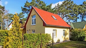 Ein zweistöckiges Haus mit rotem Dach, umgeben von Grünpflanzen und Bäumen.