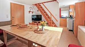 Ein kompakter Wohnbereich mit Esstisch aus Holz, einem Fernseher und einer Küchenzeile.