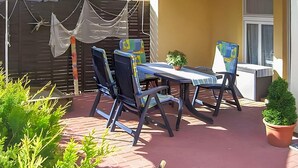 Eine Terrassenanlage im Freien mit einem Tisch und vier Stühlen, umgeben von Blumentöpfen und einem Metallgrill.
