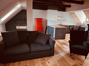 Een modern loftappartement met een donkergrijze bank, een rode deur en een keuken met witte metrotegels.