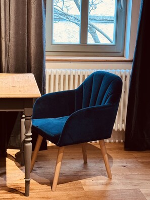 A blue chair with wooden legs and a table with a wooden top in a room with a window and curtains.