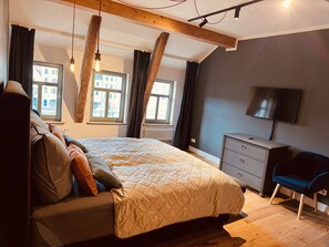 Een slaapkamer met een bed, een kapstok, een televisie en ramen voorzien van gordijnen.
