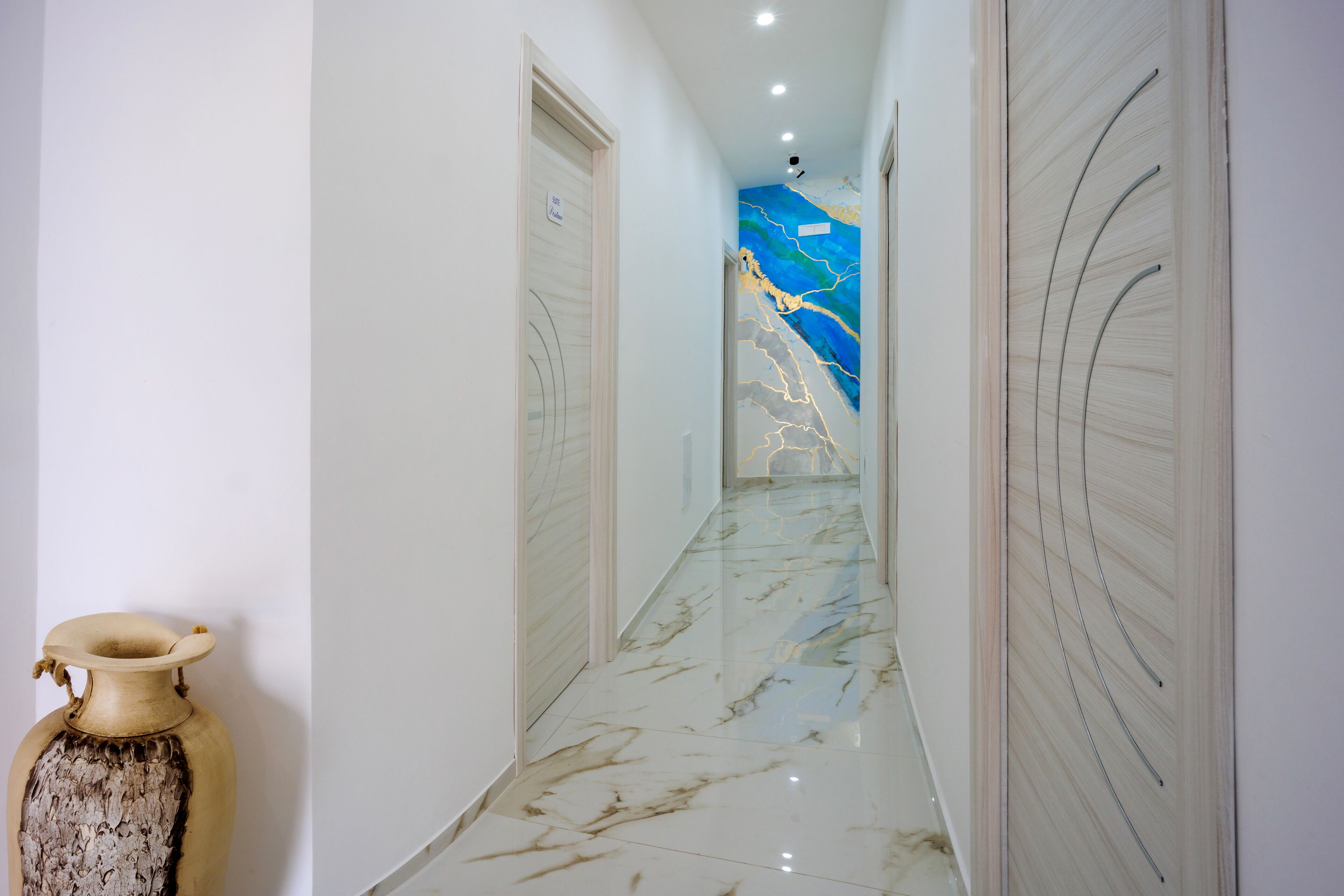Un couloir doté d’un sol en marbre, de murs blancs et d’une fresque bleue sur le mur du fond.