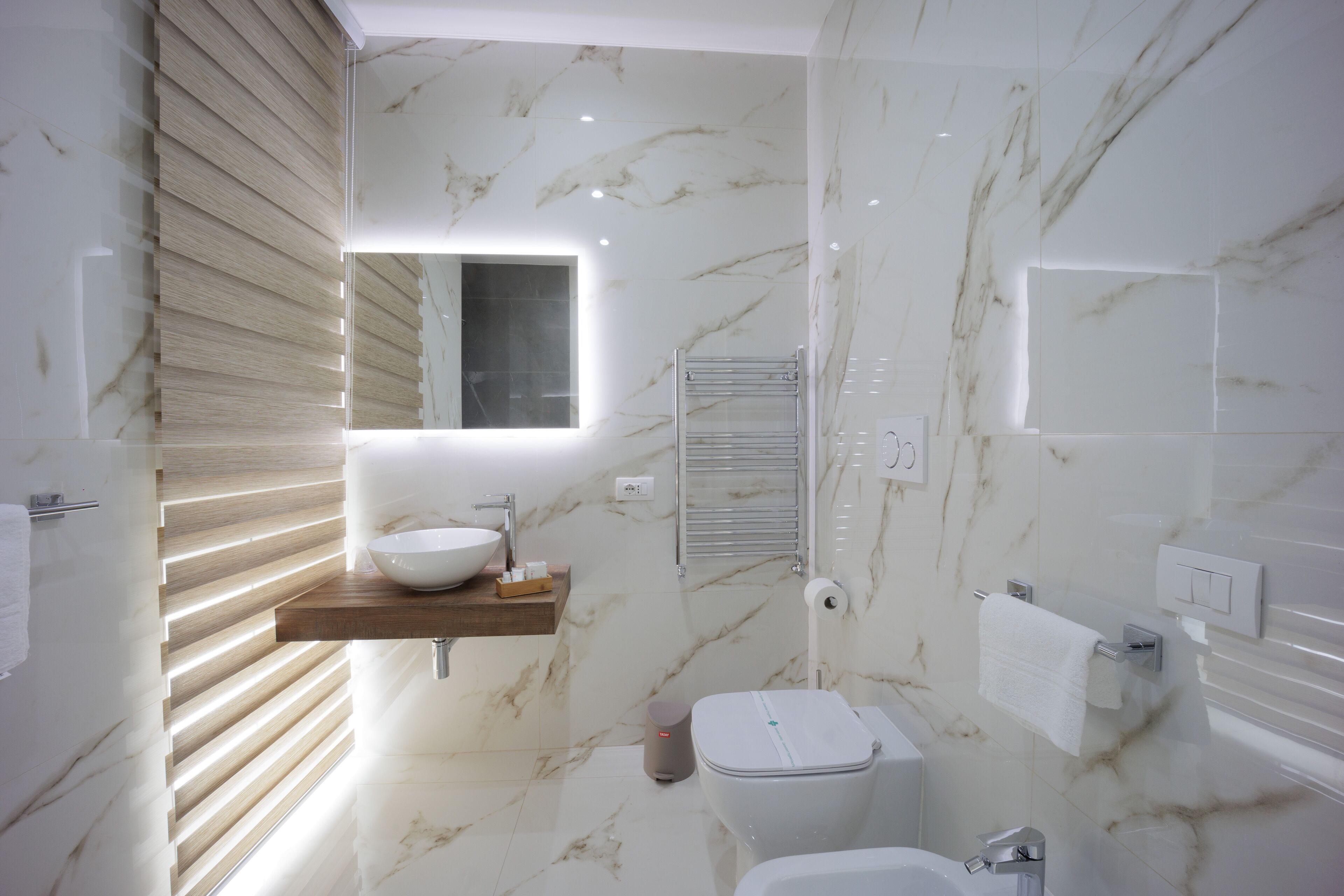 A modern bathroom with a marble floor, a wooden vanity, a white sink, and a toilet.