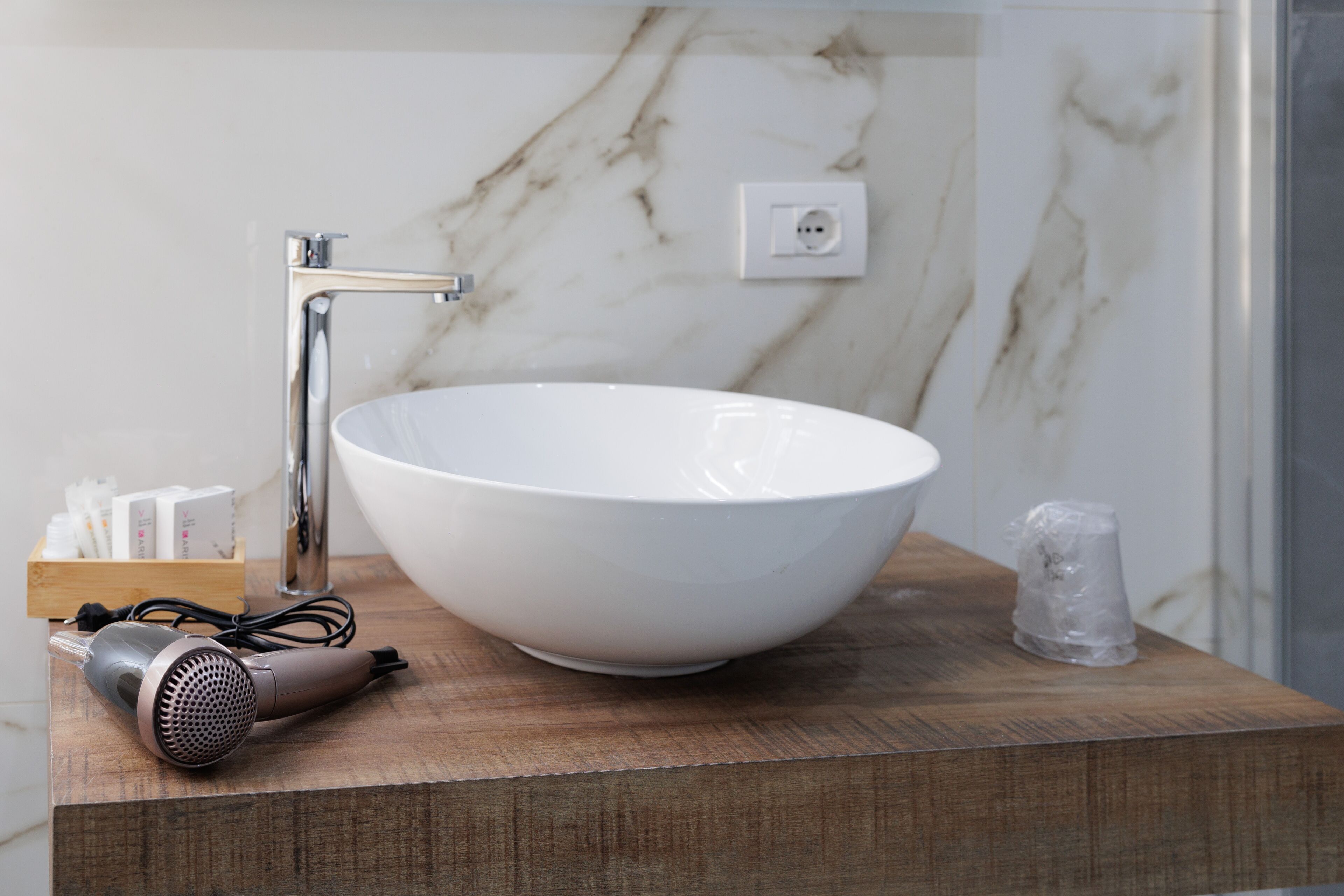 A bathroom with a large white bowl sink, a hairdryer, and a wooden countertop.