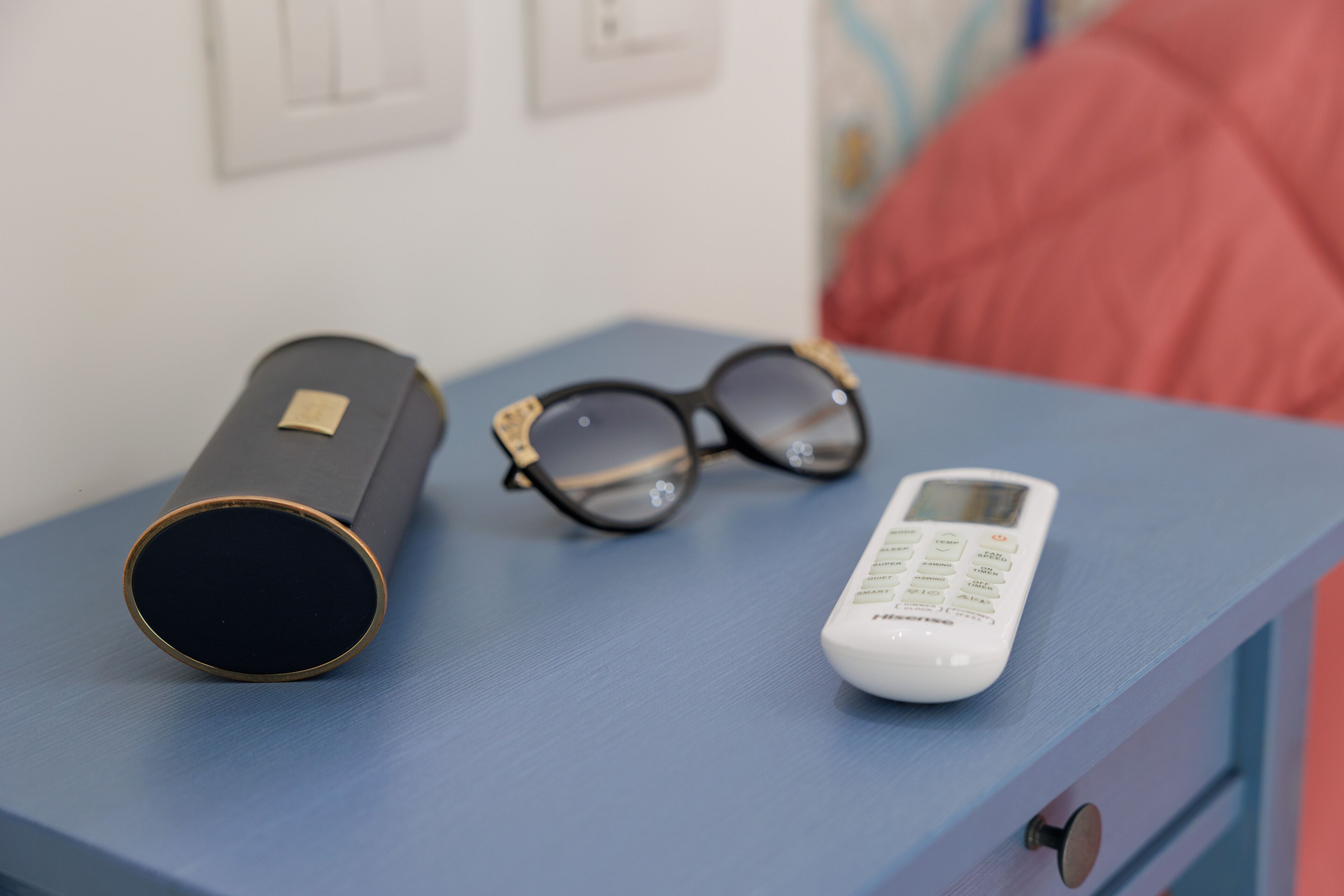 A bedside table with a pair of glasses, a remote control, and a cylindrical object.