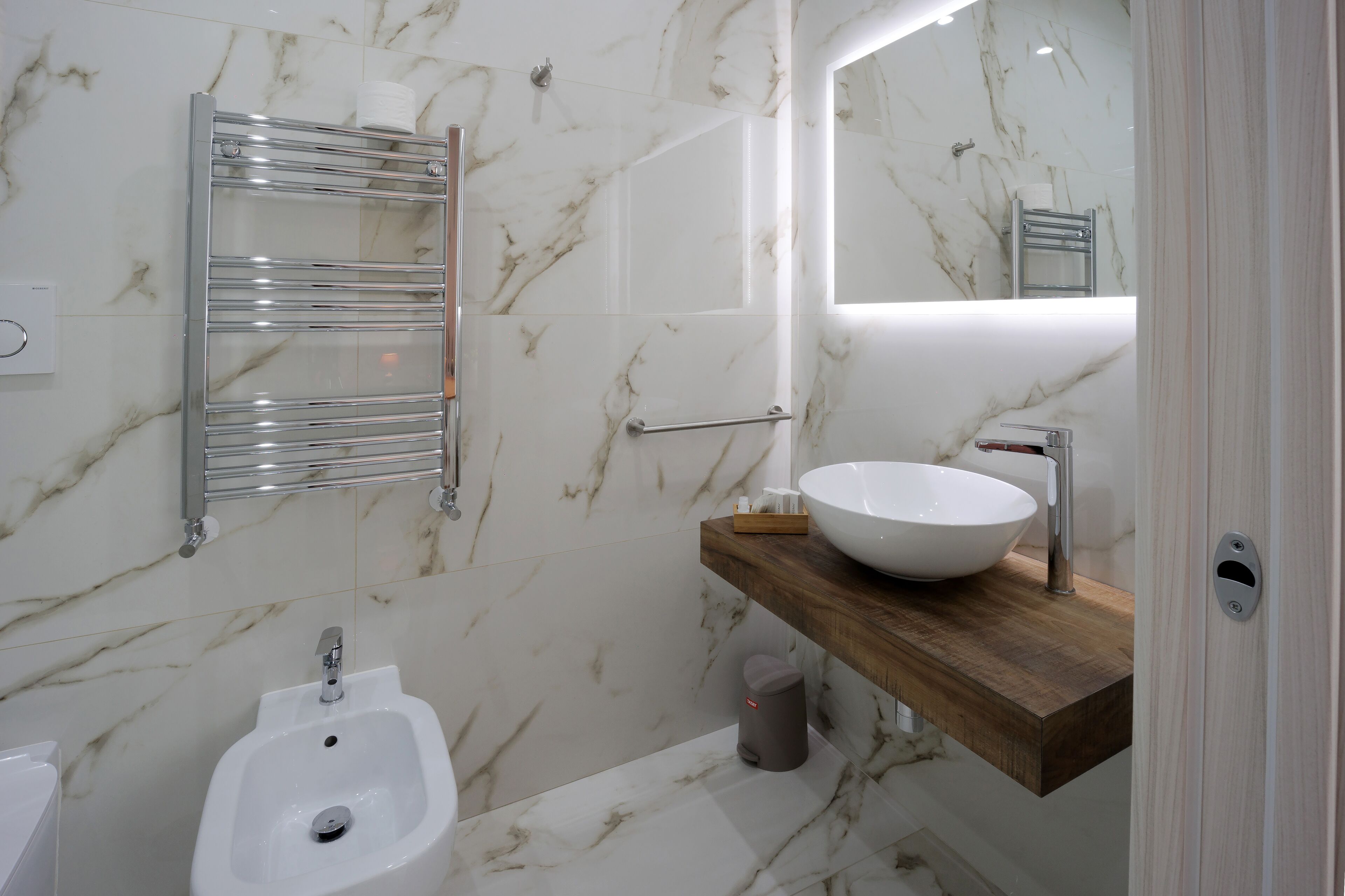 Ein modernes Badezimmer mit Marmor-Spritzschutz, einem weißen Waschbecken, einem Bidet und einer Holzwaschtisch-Möbel.