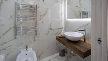 Ein modernes Badezimmer mit Marmor-Spritzschutz, einem weißen Waschbecken, einem Bidet und einer Holzwaschtisch-Möbel.