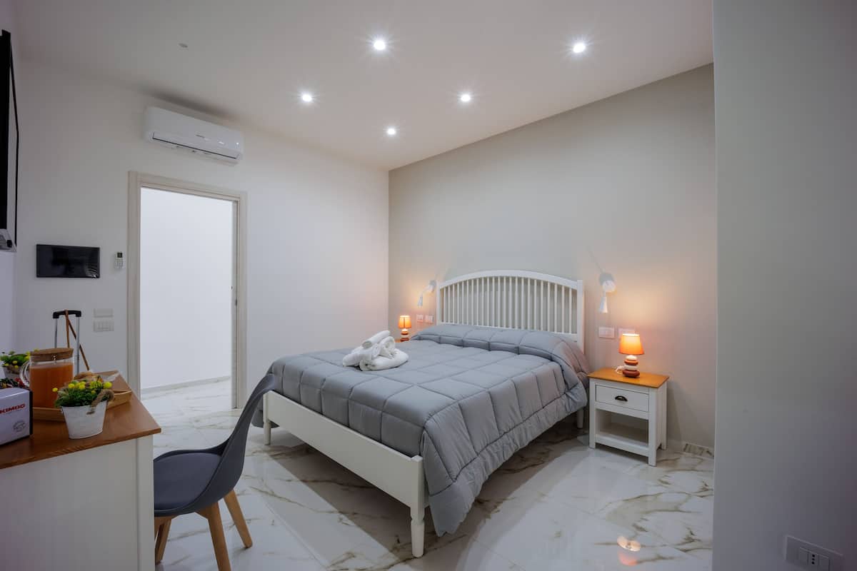 A bedroom with a bed, bedside table, chair, and a desk with a lamp.