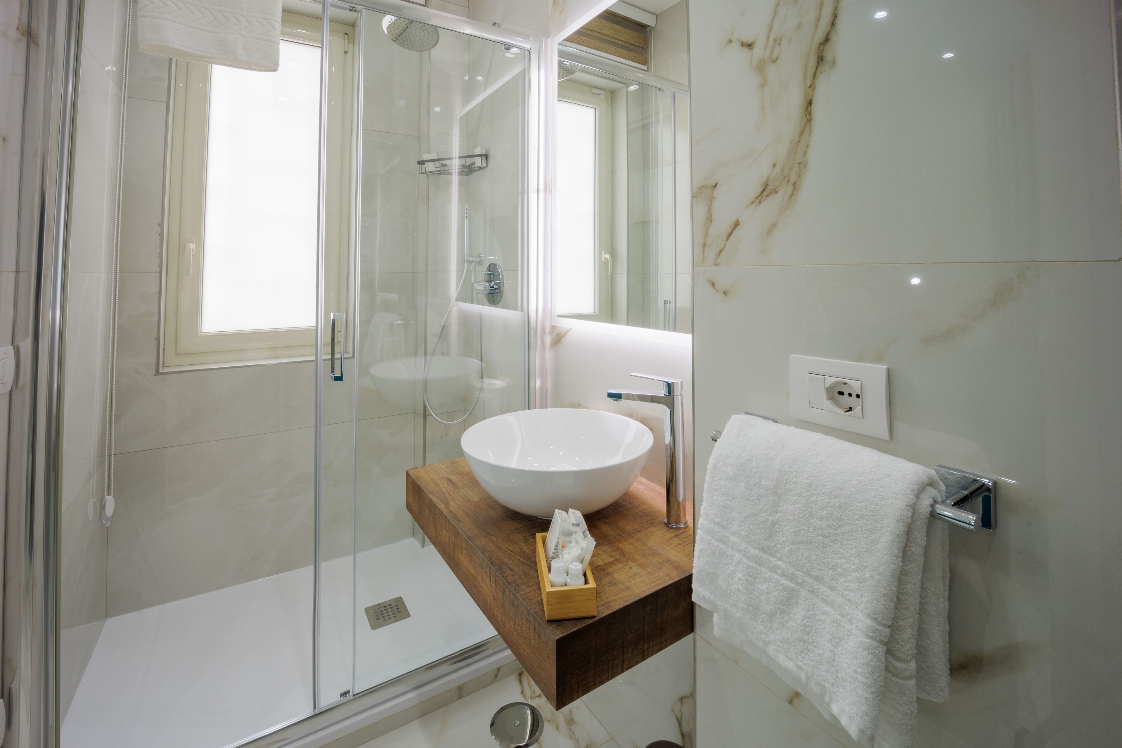 Un baño moderno con ducha envuelta en vidrio, un lavabo blanco y una encimera de madera.