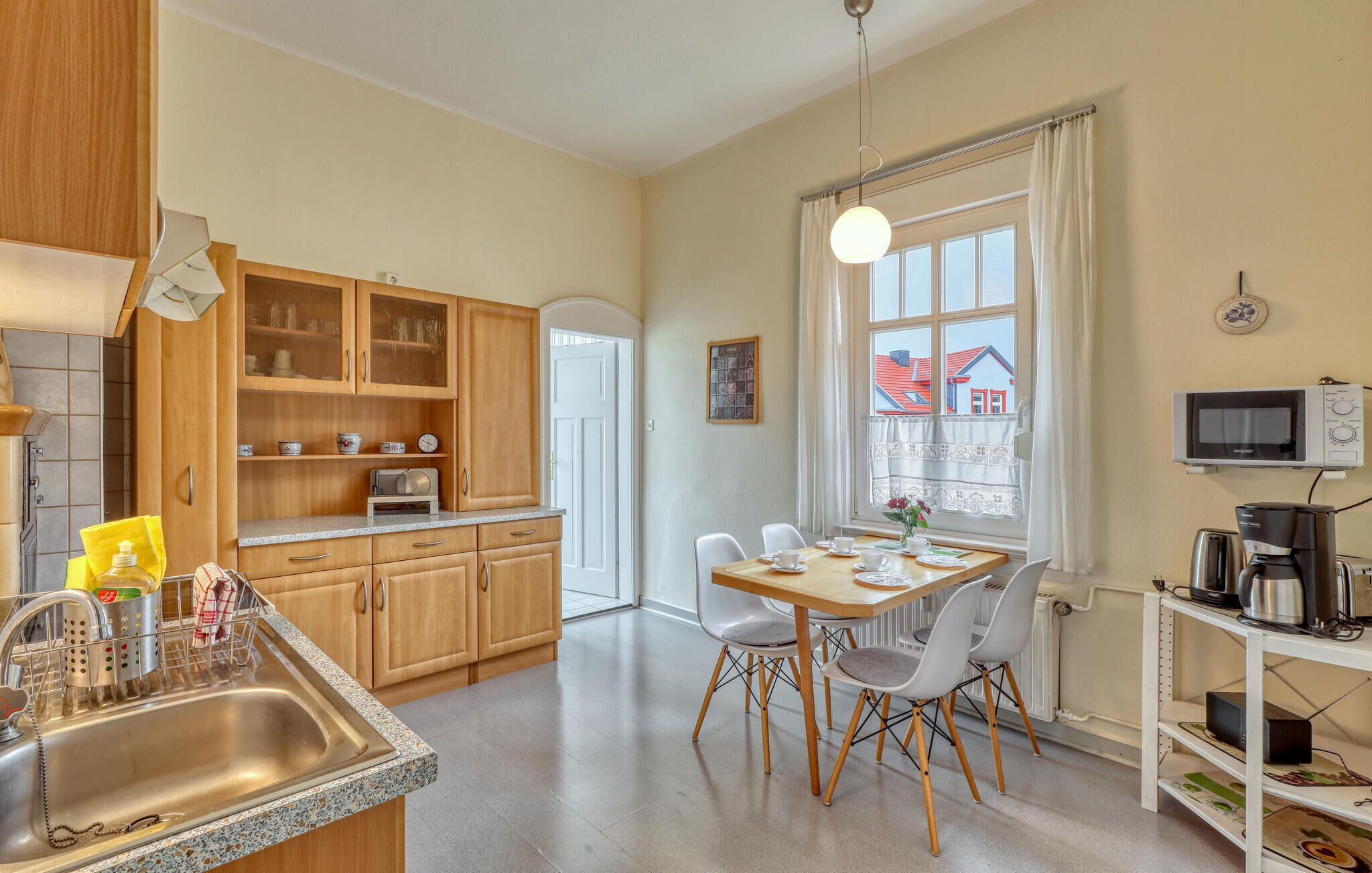 Eine moderne Küche mit Holzausstattung, einer Granit-Arbeitsplatte, einer Essecke mit Tisch und Stühlen sowie Blick auf Häuser durch ein Fenster.