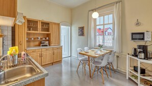 A modern kitchen with wooden cabinets, a granite countertop, a dining area with a table and chairs, and a view of houses through a window. - Ferienwohnung Friedrichroda (Friedrichroda)