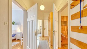 A hallway with white doors, a wooden floor, a hanging light fixture, and a wicker chair. - Ferienwohnung Friedrichroda (Friedrichroda)