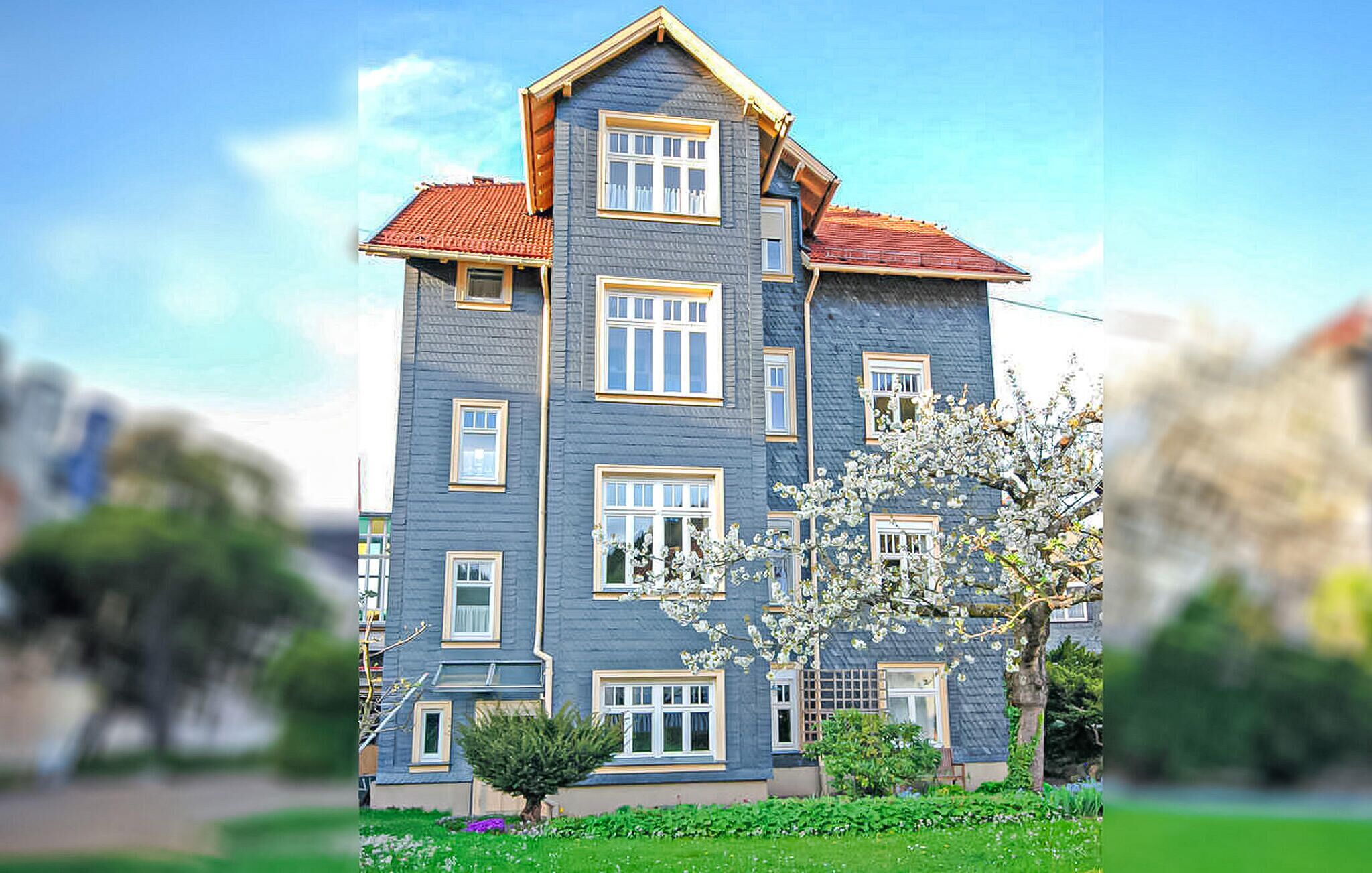 A multi-story building with a red-tiled roof, multiple windows, and a small tree in the foreground.