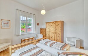 A bedroom with a bed, two bedside chairs, a wooden wardrobe, a window with curtains, and a hanging light fixture. - Ferienwohnung Friedrichroda (Friedrichroda)