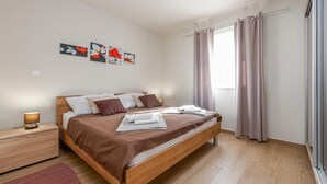 A modern bedroom with a wooden bed, a nightstand, a lamp, and artwork on the wall. - Beach front apartment in Vir with WiFi (Vir)