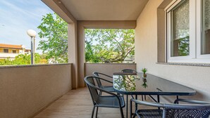 A balcony with a table and chairs, a view of trees, and a building in the background. - Beach front apartment in Vir with WiFi (Vir)