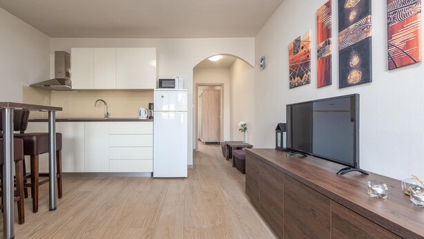 A modern kitchen with white cabinets, a microwave, and a refrigerator. There is a dining area with a table and chairs, and a TV on a wooden counter. - Beach front apartment in Vir with WiFi (Vir)