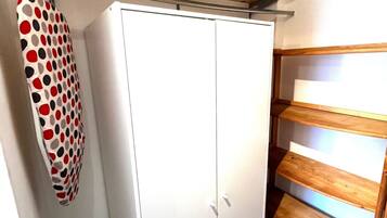 Une armoire blanche à deux portes, une étagère en bois à trois niveaux et une planche de surf fixée au mur, ornée d’un motif à pois rouges et noirs.