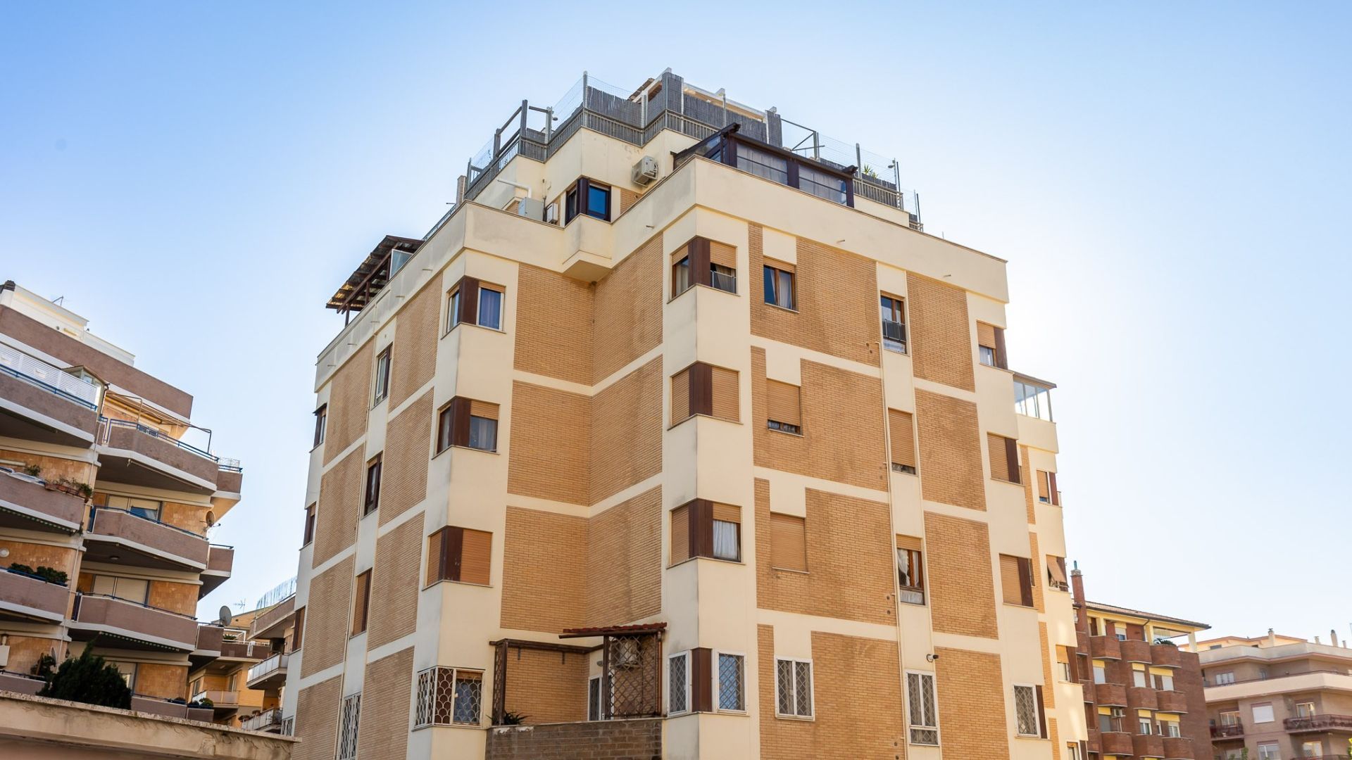 Un edificio residenziale a più piani con un design architettonico moderno, caratterizzato da balconi e una terrazza sul tetto.