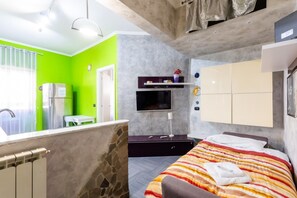 A modern hotel room with a stone accent wall, a bed with striped bedding, a TV, a small table, and a green wall.
