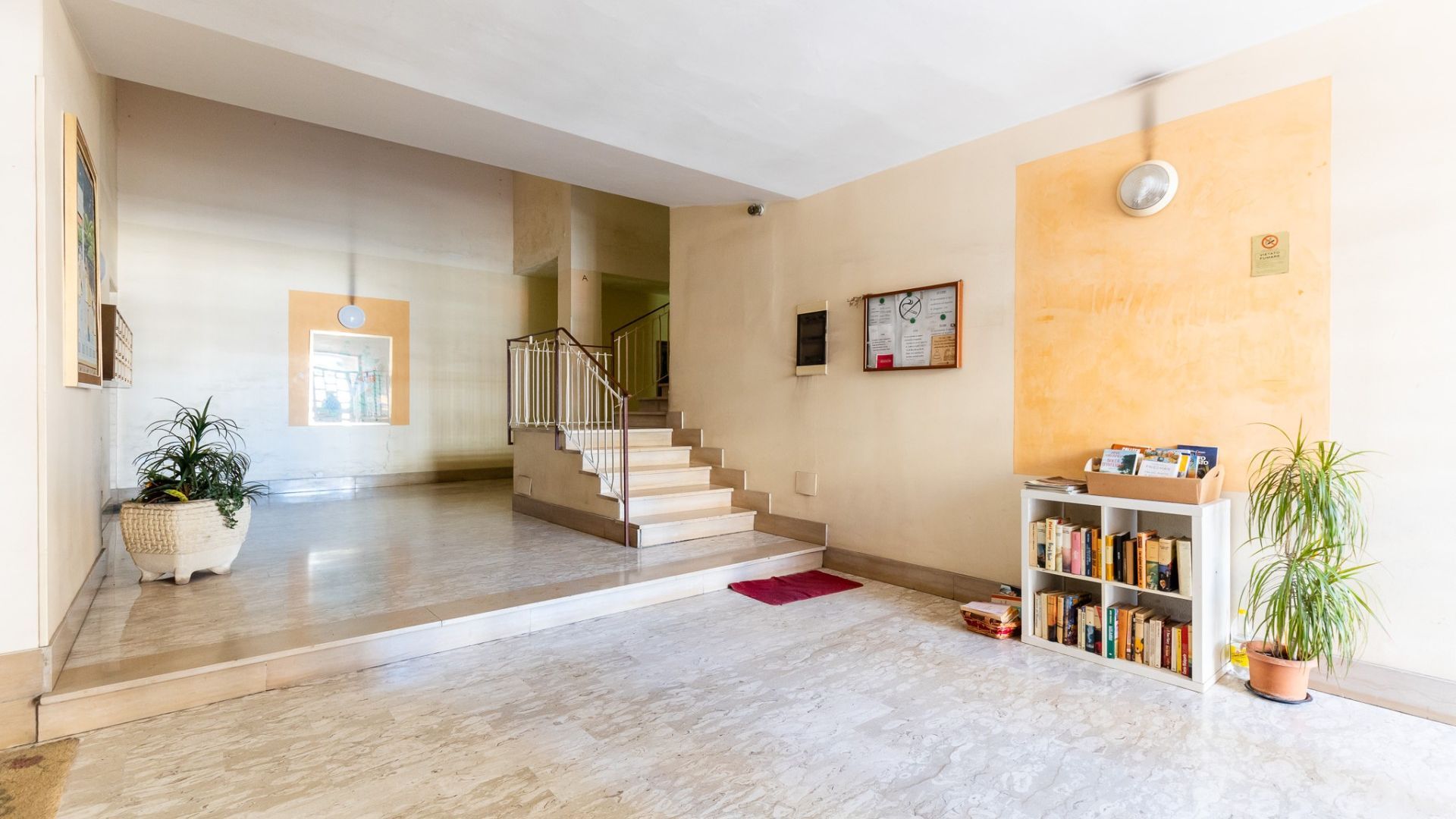A spacious hallway with a staircase, a bookshelf, and a potted plant.