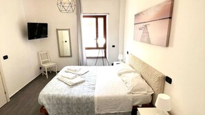 Una camera d'albergo con un letto, una sedia, una televisione, uno specchio e un quadro appeso al muro.