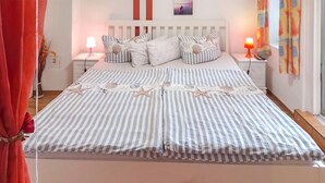Ein Bett mit gestreifter Bettwäsche und Sternfisch-Motiven, zwei Nachttische mit Lampen sowie eine Wand mit einem gerahmten Bild.