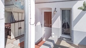 Ein kleiner, abgeschlossener Balkon mit einem Korbstuhl, einer Holztür und einer kleinen Laterne.
