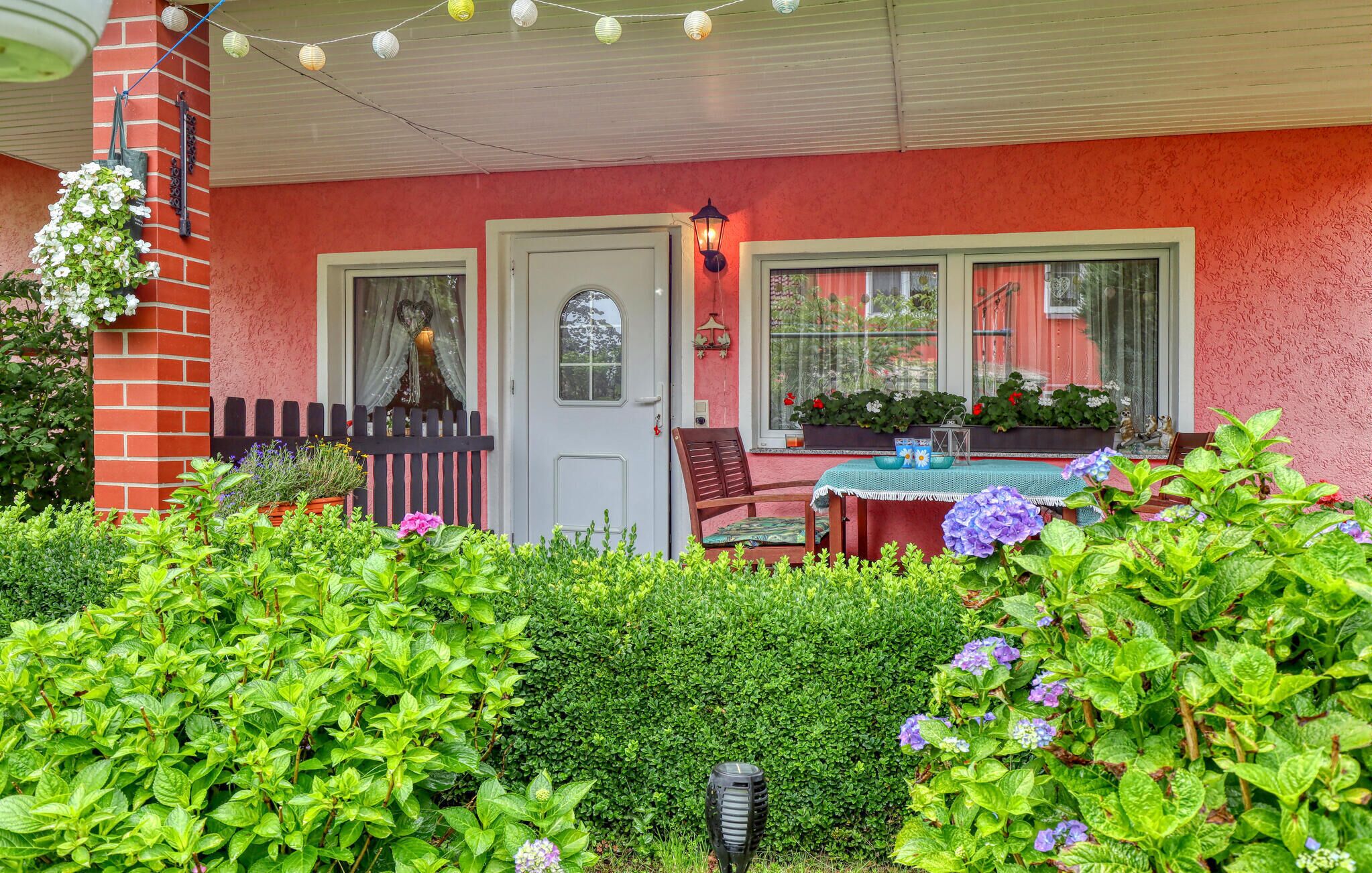 A covered porch with a table and chairs, surrounded by lush greenery and potted plants.