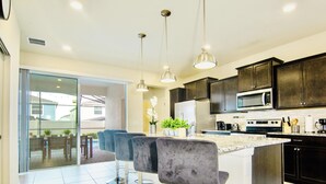 Una cocina moderna con armarios oscuros, una isla central con taburetes altos y un amplio ventanal con vistas a un jardín trasero.