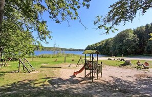 Un terrain de jeux avec un toboggan et des balançoires, entouré d’arbres et offrant une vue sur un lac.