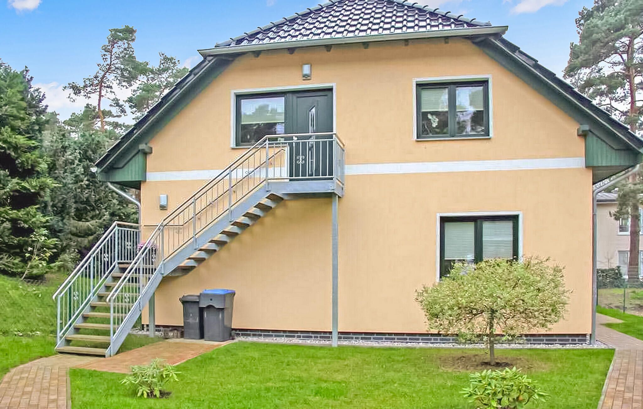 A two-story house with a staircase leading to the upper floor, a small garden with a tree, and a paved driveway.