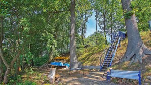 Un parque con un banco de madera, una escalera azul y un paraguas amarillo.