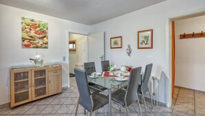 A dining area with a glass table and chairs, a wooden cabinet with glass doors, and a kitchen area visible in the background. - 2 bedroom lovely apartment in Mirow (Mirow)