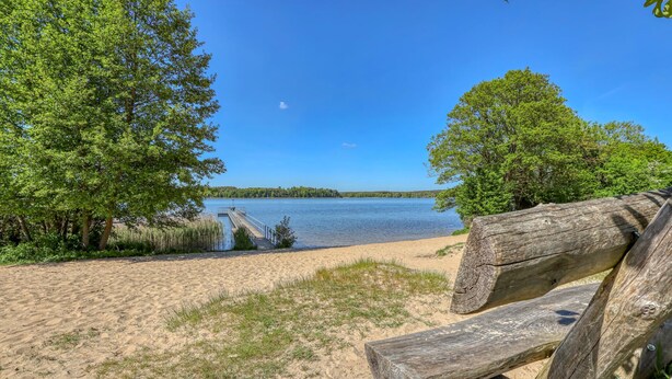 A sandy beach with a wooden dock extending into a calm lake, surrounded by dense green trees. - 2 bedroom lovely apartment in Mirow (Mirow)