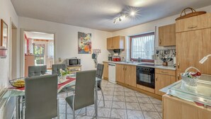 A modern kitchen with wooden cabinets, a dining area with a glass table and chairs, and a view of the outdoors. - 2 bedroom lovely apartment in Mirow (Mirow)