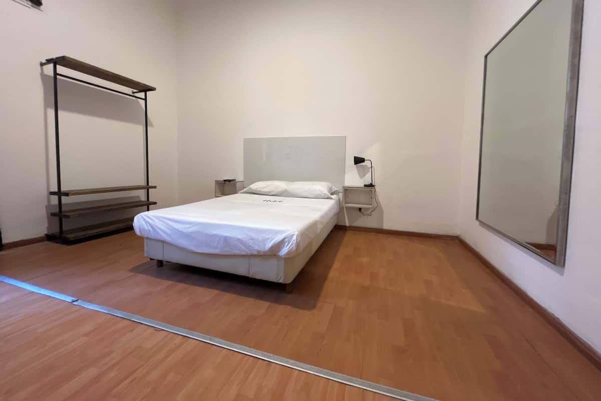 A bedroom with a bed, bedside table, lamp, and a large mirror.