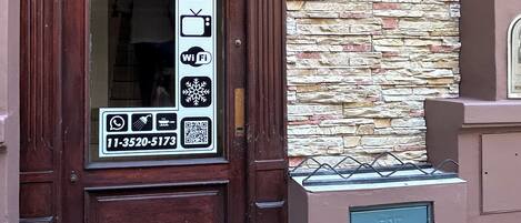 Una puerta de madera con un cartel que indica servicios como Wi-Fi, un televisor y un icono de casa, sugiriendo una propiedad de alquiler.