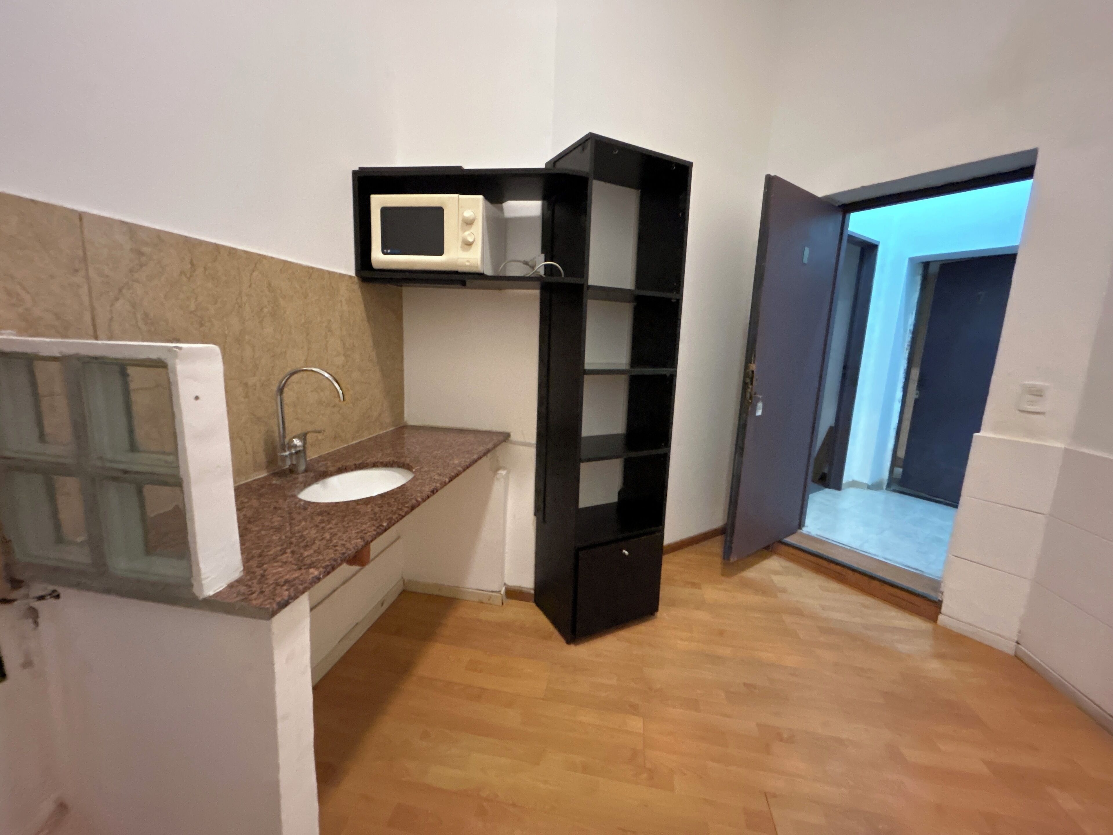 A compact kitchen with a white sink, a microwave, and a black shelving unit.