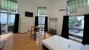 Ein Hotelzimmer mit einem Bett, einem Schreibtisch mit Stuhl, einem Fernseher und großen Fenstern mit Vorhängen.