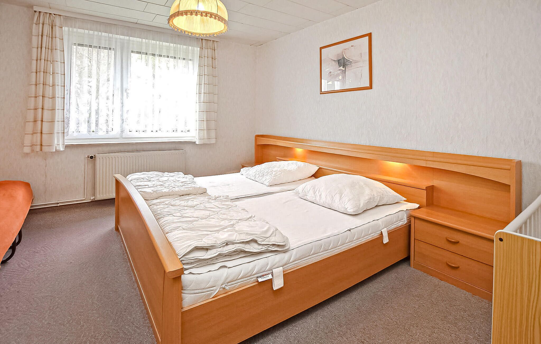 Une chambre à coucher avec un lit en bois, du linge de lit blanc, un radiateur, une fenêtre avec des rideaux, une chaise et une table de chevet.